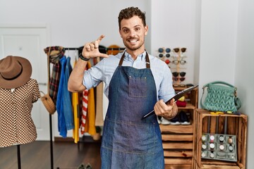 Canvas Print - Handsome young man working as manager at retail boutique smiling and confident gesturing with hand doing small size sign with fingers looking and the camera. measure concept.