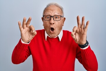 Poster - Senior man with grey hair standing over isolated background looking surprised and shocked doing ok approval symbol with fingers. crazy expression