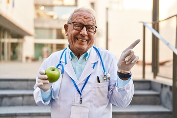 Sticker - Senior doctor with grey hair holding healthy green apple smiling happy pointing with hand and finger to the side