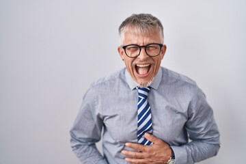 Poster - Hispanic business man with grey hair wearing glasses smiling and laughing hard out loud because funny crazy joke with hands on body.