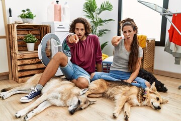 Wall Mural - Young hispanic couple doing laundry with dogs pointing displeased and frustrated to the camera, angry and furious with you