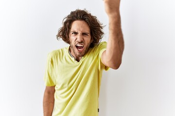 Poster - Young hispanic man standing over isolated background angry and mad raising fist frustrated and furious while shouting with anger. rage and aggressive concept.