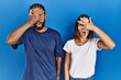 Young hispanic couple standing together peeking in shock covering face and eyes with hand, looking through fingers with embarrassed expression.