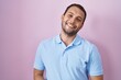 © Krakenimages.com - Hispanic man standing over pink background with hands together and crossed fingers smiling relaxed and cheerful. success and optimistic