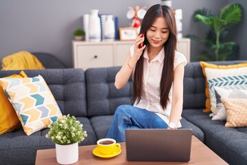 Sticker - Young chinese woman talking on smartphone using laptop at home