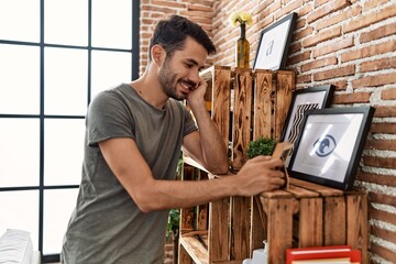 Wall Mural - Young hispanic man smiling confident looking picture frame at home