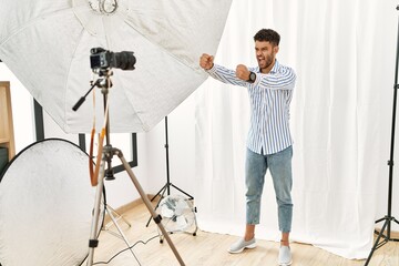 Wall Mural - Arab young man posing as model at photography studio angry and mad raising fists frustrated and furious while shouting with anger. rage and aggressive concept.