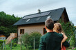 © Halfpoint - Rear view of dad holding her little girl in arms and looking at their house with installed solar panels. Alternative energy, saving resources and sustainable lifestyle concept.