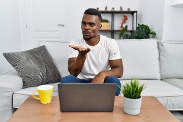 Sticker - Young african man using laptop at home looking at the camera blowing a kiss with hand on air being lovely and sexy. love expression.