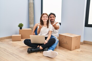 Sticker - Young couple using laptop at new home smiling cheerful offering palm hand giving assistance and acceptance.