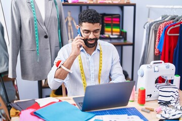 Poster - Young arab man tailor talking on smartphone using laptop at tailor shop