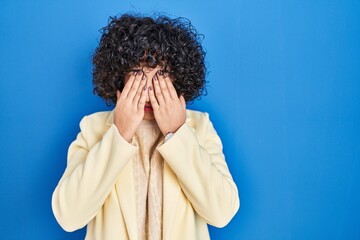 Sticker - Young brunette woman with curly hair standing over blue background rubbing eyes for fatigue and headache, sleepy and tired expression. vision problem