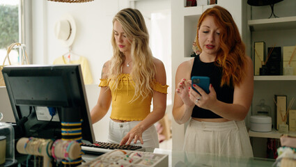 Sticker - Two women shop employees using smartphone and computer working at clothing store