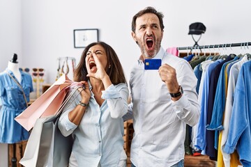 Poster - Hispanic middle age couple holding shopping bags and credit card shouting and screaming loud to side with hand on mouth. communication concept.