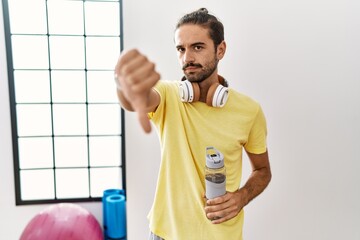 Canvas Print - Young hispanic man wearing sportswear and drinking water at the gym looking unhappy and angry showing rejection and negative with thumbs down gesture. bad expression.