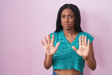 Young african american with braids standing over pink background moving away hands palms showing refusal and denial with afraid and disgusting expression. stop and forbidden.