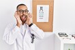 © Krakenimages.com - African american optician man standing by eyesight test smiling cheerful playing peek a boo with hands showing face. surprised and exited