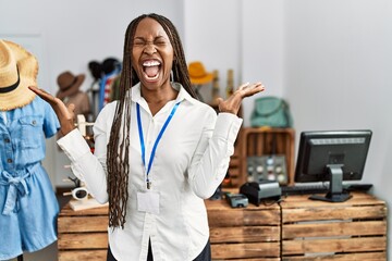 Poster - Black woman with braids working as manager at retail boutique crazy and mad shouting and yelling with aggressive expression and arms raised. frustration concept.