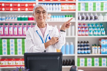 Canvas Print - Middle age woman with tattoos working at pharmacy drugstore with a big smile on face, pointing with hand finger to the side looking at the camera.