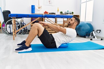 Canvas Print - Young hispanic man patient having back rehab session using fit ball at clinic