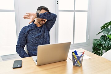 Poster - Young hispanic man with beard working at the office with laptop covering eyes with arm, looking serious and sad. sightless, hiding and rejection concept