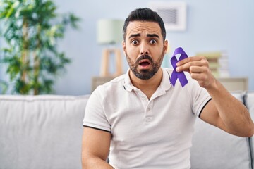 Poster - Young hispanic man with beard holding purple ribbon awareness scared and amazed with open mouth for surprise, disbelief face