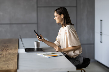 Young pretty woman use a laptop to work in the kitchen use the phone