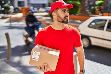 Canvas Print - Young hispanic man courier holding package at street