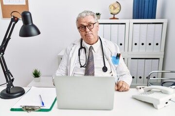 Wall Mural - Senior caucasian man wearing doctor uniform and stethoscope at the clinic smiling looking to the side and staring away thinking.