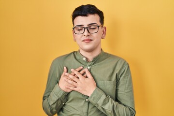 Canvas Print - Non binary person standing over yellow background smiling with hands on chest with closed eyes and grateful gesture on face. health concept.