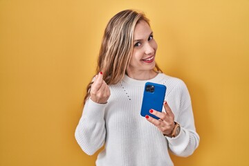 Sticker - Young blonde woman using smartphone typing message doing money gesture with hands, asking for salary payment, millionaire business