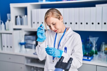 Canvas Print - Young blonde woman scientist pouring liquid on test tube at laboratory