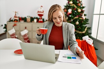 Young caucasian woman drinking coffee working sitting by christmas tree at home