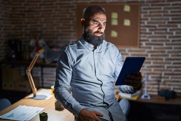 Wall Mural - Young hispanic man with beard and tattoos working at the office at night skeptic and nervous, frowning upset because of problem. negative person.