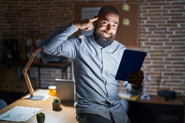 Canvas Print - Young hispanic man with beard and tattoos working at the office at night smiling pointing to head with one finger, great idea or thought, good memory