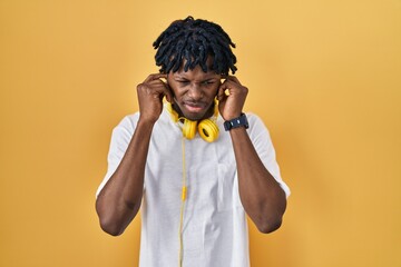 Sticker - Young african man with dreadlocks standing over yellow background covering ears with fingers with annoyed expression for the noise of loud music. deaf concept.