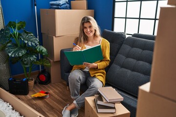 Sticker - Young blonde woman smiling confident writing on book at new home