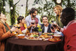 © Lomb - Company of happy people chatting dining at the barbecue table relaxing together eating grilled food and drinking wine