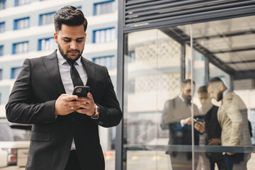 Wall Mural - Portrait of a business man outdoors using the phone against the backdrop of a glass building downtown.