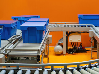Poster - Warehouse of courier company. Conveyor lines with blue boxes. Warehouse conveyor in orange room. Production line for courier parcels. Blue plastic boxes are moving along conveyor. Courier business