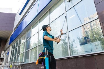 An employee of a professional cleaning service in overalls washes the glass of the windows of the facade of the building. Showcase cleaning for shops and businesses