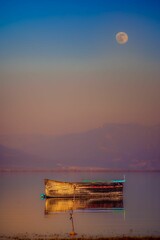 vertical shot of a boat on lake kerkini, greece on a pink sky background under the full moon.