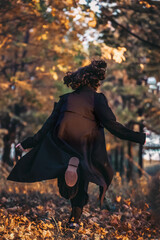 girl in black raincoat runs down an alley in city park against the background of autumn maple trees, rear view, dark academy subculture theme, autumn tinting, autumn background, selective focus