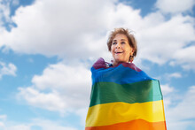 Older Lady Smiling, Surrounded By The Rainbow Colored Flag Representing The Gay Community. Gay Pride Day. Fight For Equality, Freedom And Gay Rights