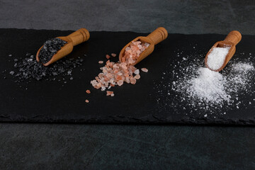 different types of salt. white sea, pink himalayan and black volcanic salt on three wooden spoons.