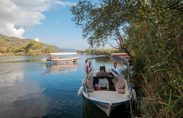 Wall Mural - The rock-cut temple tombs of the ancient city of Kaunos in Dalyan, Muğla, Turkey. Beautiful view of Dalyan river with reed beds, excursion boats and carved tombs in the background.