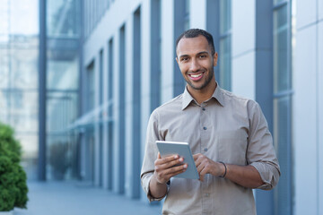 Portrait of a happy businessman outside an office building, a man in a casual shirt is looking at the camera and smiling, a businessman is using a tablet computer.