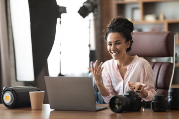 Wall Mural - Emotional millennial woman photographer having business call, using laptop