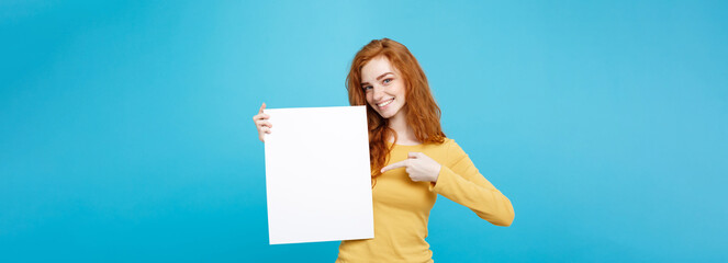 Wall Mural - Close up Portrait young beautiful attractive ginger red hair girl smiling showing blank sign. Blue Pastel Background. Copy space.