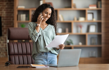 Wall Mural - Happy brunette woman having phone conversation, reading documents